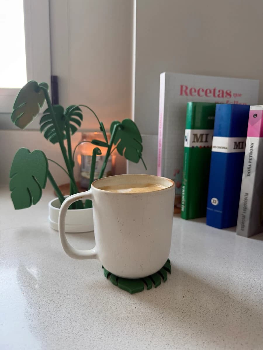 Posavasos con silueta de hojas de Monstera recogidos en maceta junto a taza de café